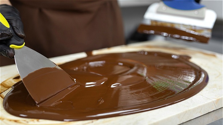 Tempered chocolate being spread out on a marble board