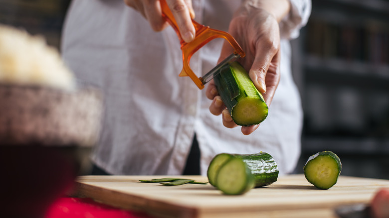 peeling cucumber into strips over cutting board