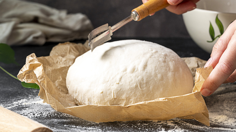 Scoring a loaf of bread with a scoring tool 