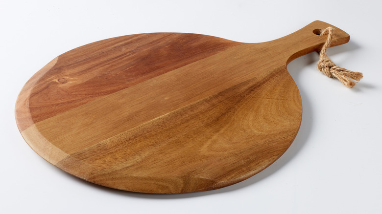 A round wooden cheese board with a handle on a white background