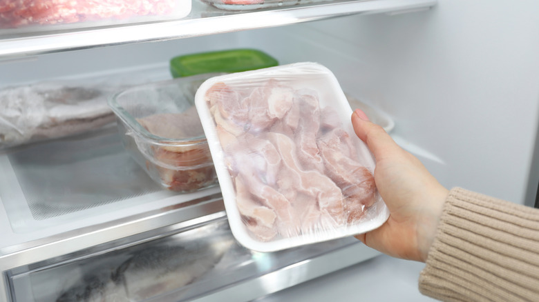 A hand holding frozen meat in front of a fridge containing other items