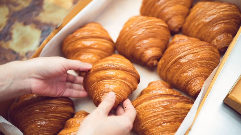 hands grabbing croissant from box