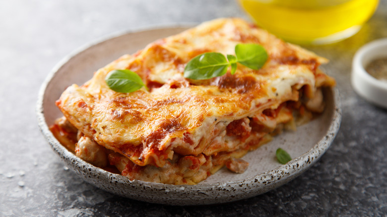 A slice of lasagna with red sauce, ground turkey meat, and a green vegetable garnish on top