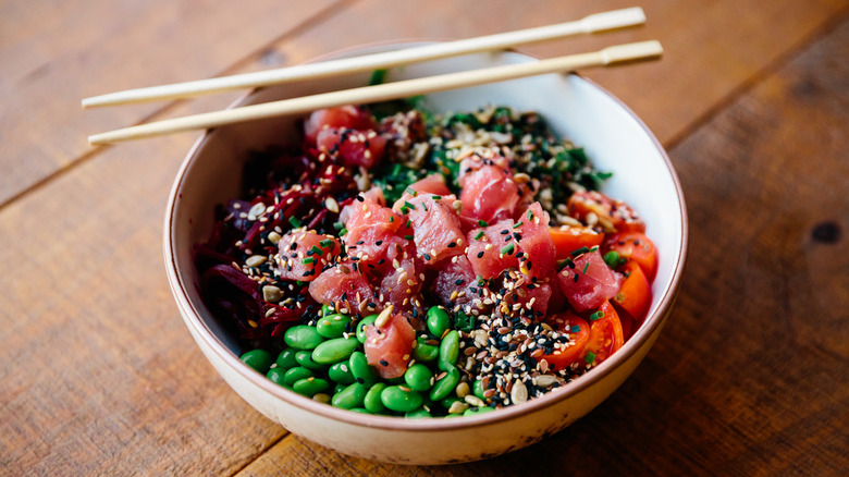 A tuna poke bowl on a wooden table with chopsticks