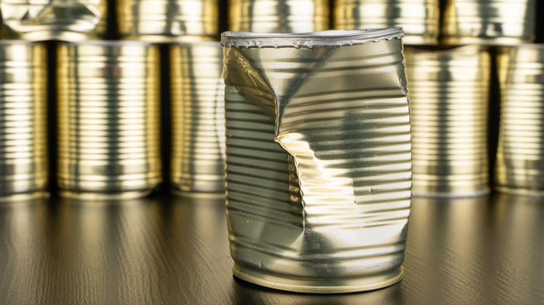 Dented and damaged aluminum can in front of normal cans