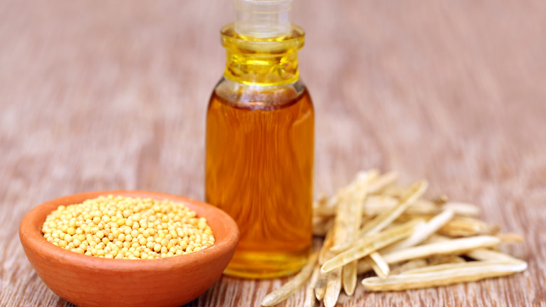 A small glass bottle of mustard oil next to mustard seeds