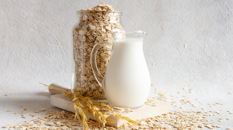 glass jar full of cut oats next to a glass pitcher of oat milk