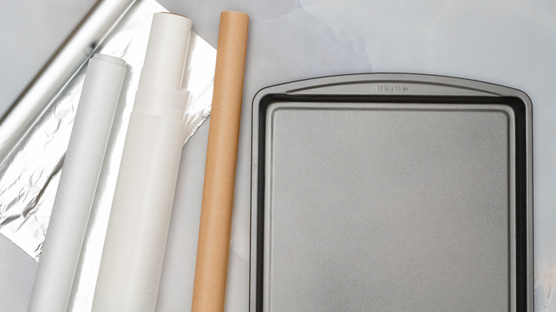 aluminum foil, parchment paper, and wax paper rolls next to a baking sheet