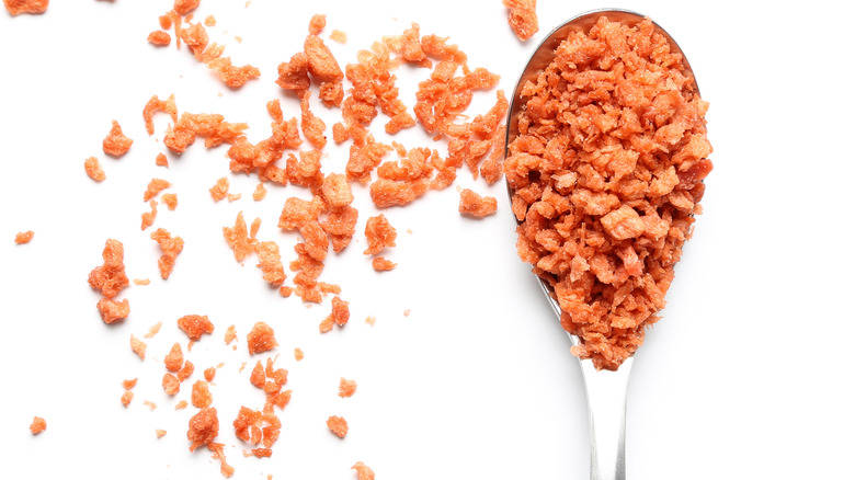 A pile of bacon bits on a white background and on spoon