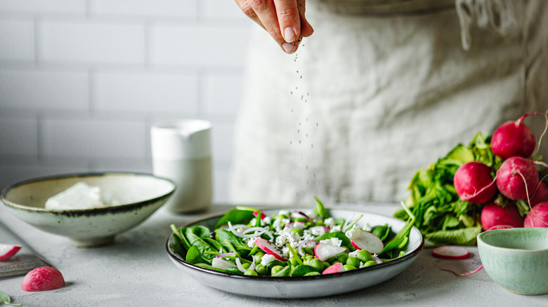 Hand adding pepper to salad