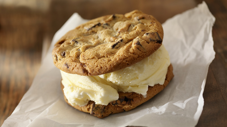 An ice cream sandwich made from cookies and vanilla soft serve rests on some parchments paper