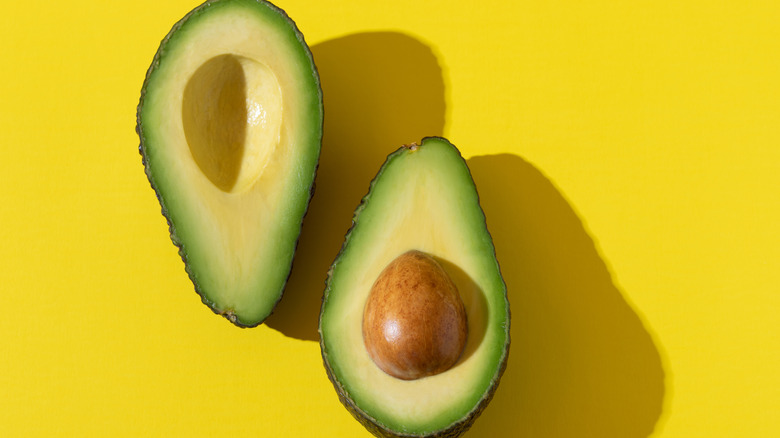 An avocado sliced in half on a yellow background