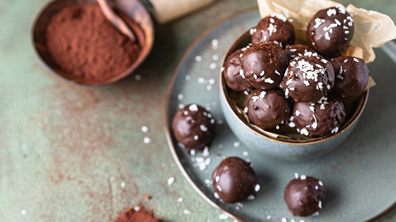 Chocolate peanut butter balls sprinkled with flake salt next to a container of cocoa powder