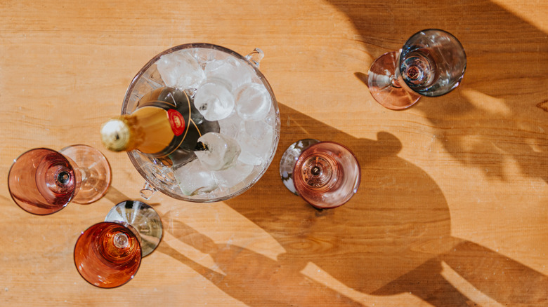 Overhead shot of a bottle of Champagne in an ice bucket with glasses of Champagne on wood table