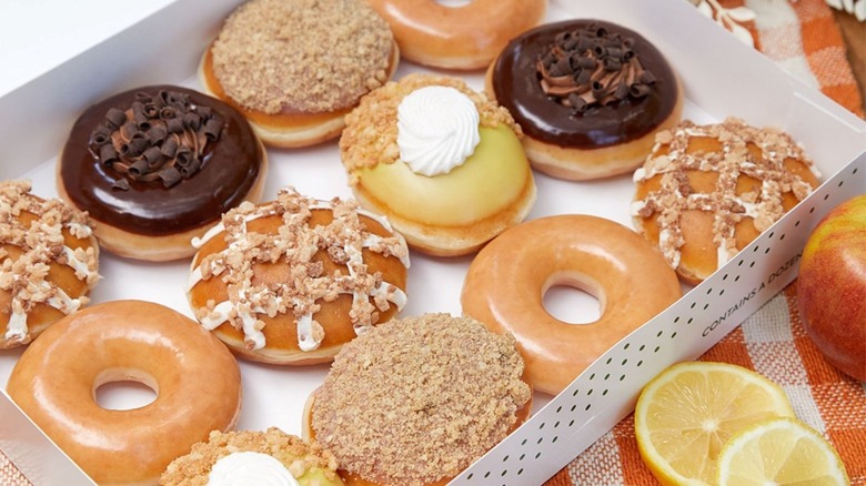 Krispy Kreme Thanksgiving donuts in open box with autumnal fruits nearby