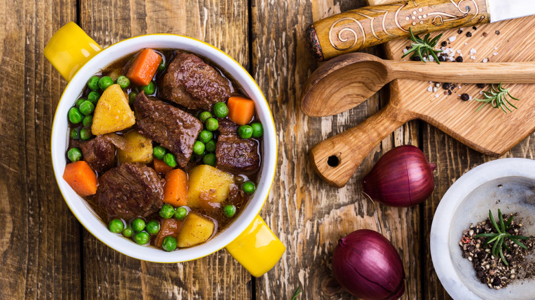 Beef stew with with potatoes, carrots and peas on a rustic table.