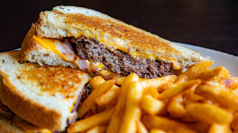Cheesy beef patty melts with fries on a ceramic plate.