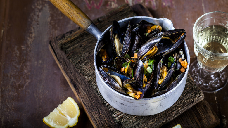 Saucepan filled with cooked mussels sitting on a wooden cutting board