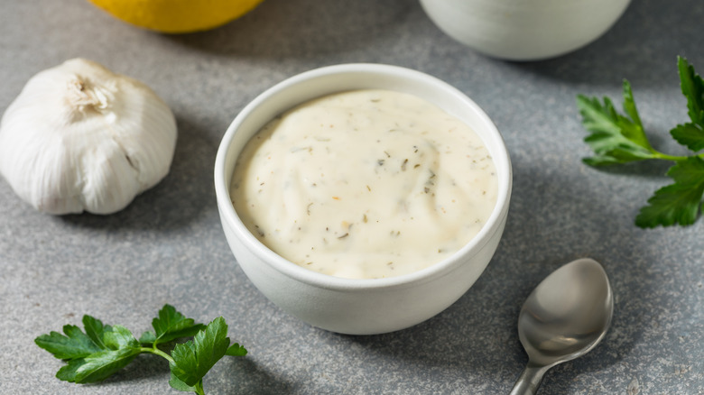 White ramekin of ranch dressing surrounded by fresh parsley and a whole head of garlic