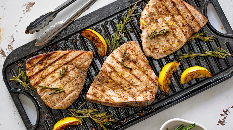 Swordfish steaks on an indoor grill with rosemary sprigs and lemon wedges