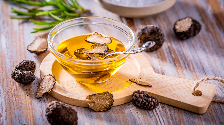 Oil in a bowl infused with slices of truffles and surrounded by truffles