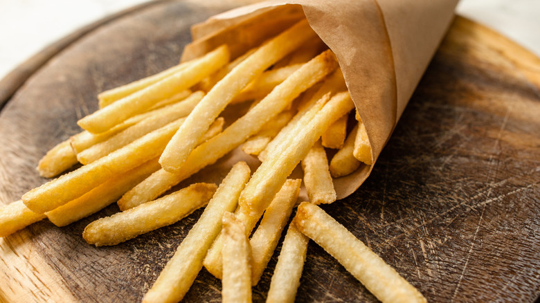 Paper cone of fast food fries spilling onto a wood board