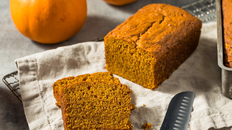 A loaf of pumpkin bread with two slices next to a pumpkin