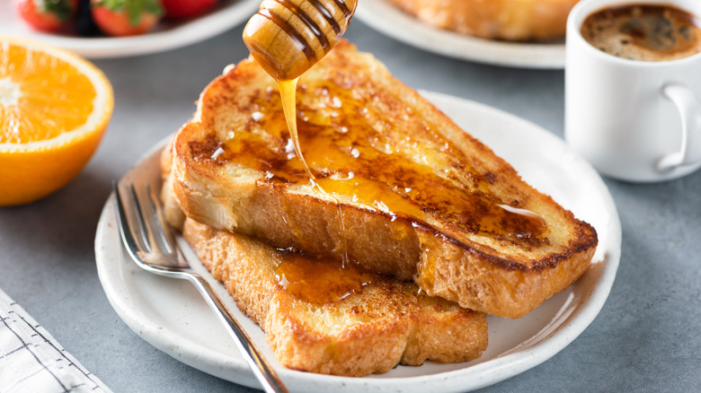 Two slices of french toast on a plate with honey being drizzled on top