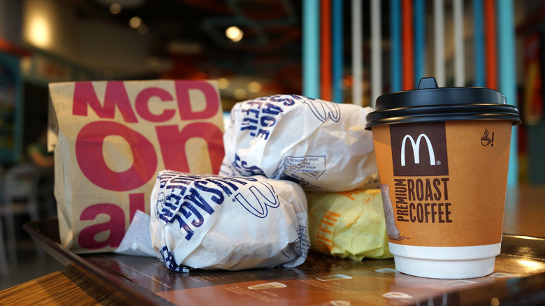 A pile of Sausage McMuffins with Egg and one Egg McMuffin, with a cup of coffee and a McDonald's bag