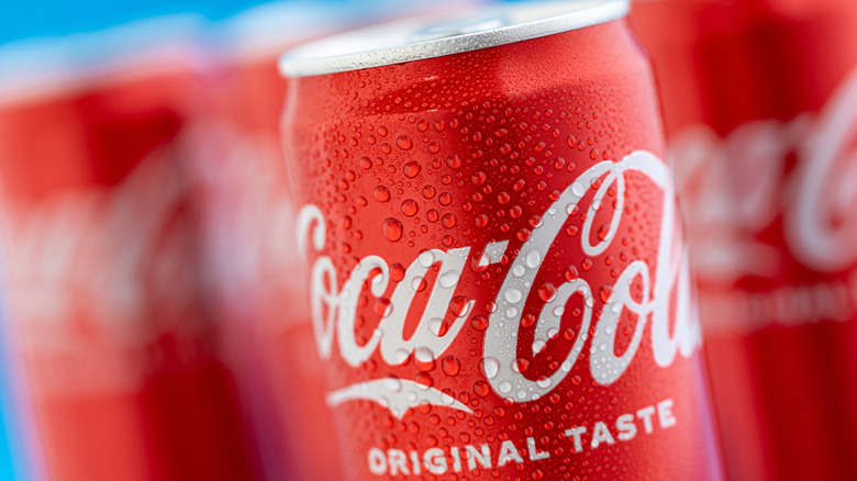 Close-up of Coca-Cola Original Taste can with more blurred cans in the background
