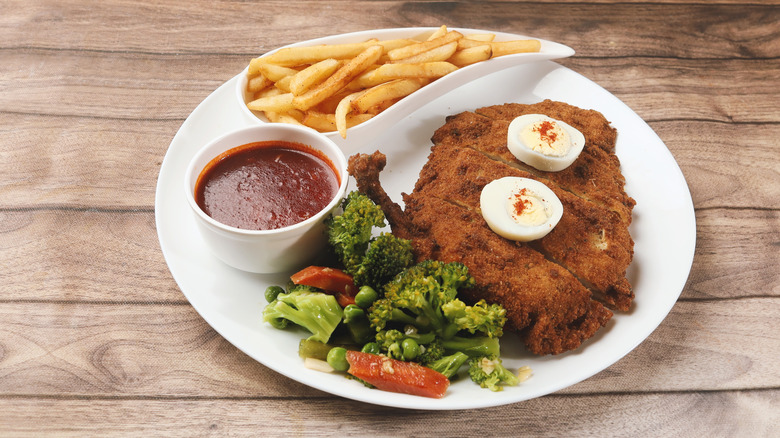 Maryland fried chicken garnished with a halved hard-boiled egg and served with fries, vegetables, and a red sauce on a white plate
