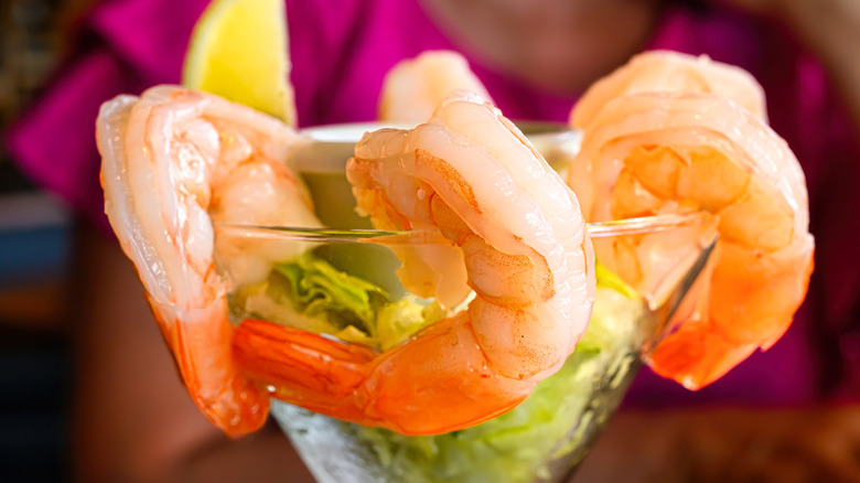 Classic shrimp cocktail in a tulip glass with a lemon wedge and iceberg lettuce