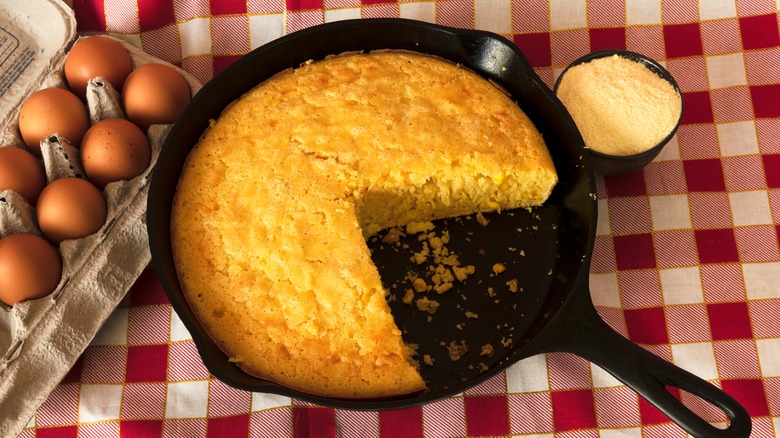 Cornbread in cast iron skillet with wedge missing.