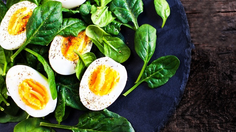 Boiled eggs with spinach leaves on black plate