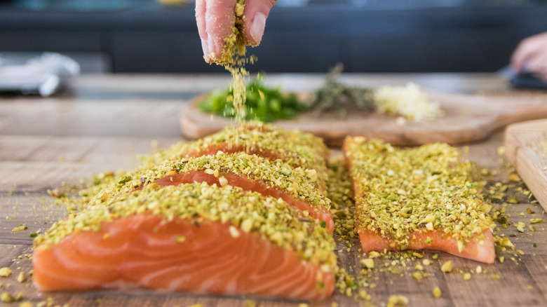 hand sprinkling seasoning on salmon