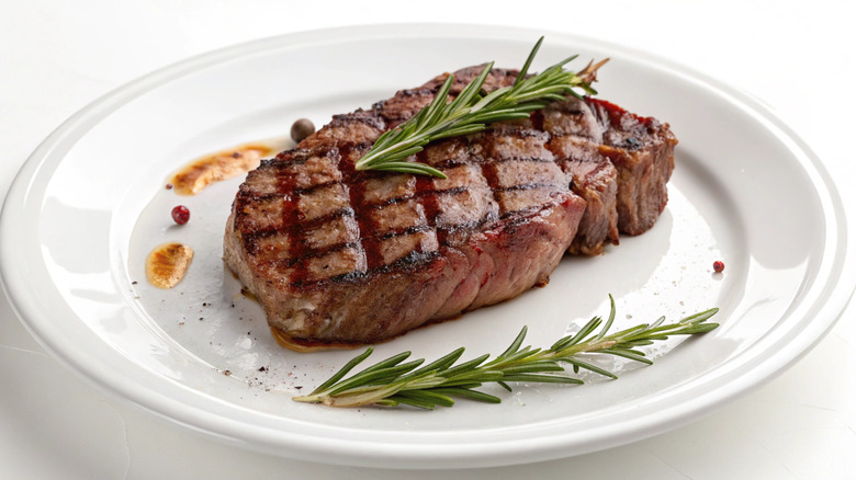 A piece of steak with some greenery on a white plate
