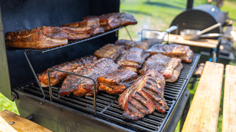 Varying cuts of meat inside of a black smoker outdoors