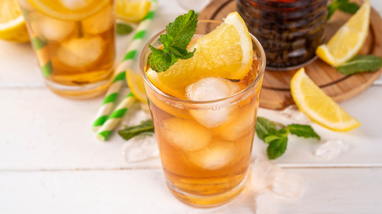 A glass of tea and bourbon with a lemon wedge and mint leaves
