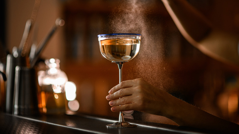 Glass with tall metal stem on a bar, filled with a bubbly cocktail