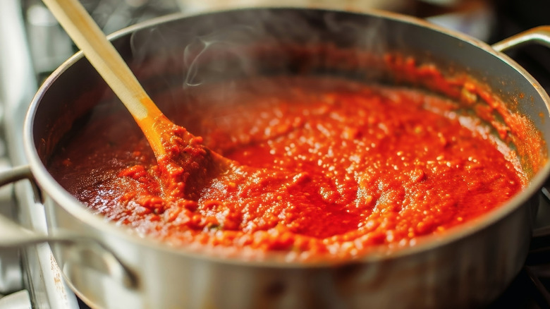 A pan of simmering tomato sauce with a wooden spoon