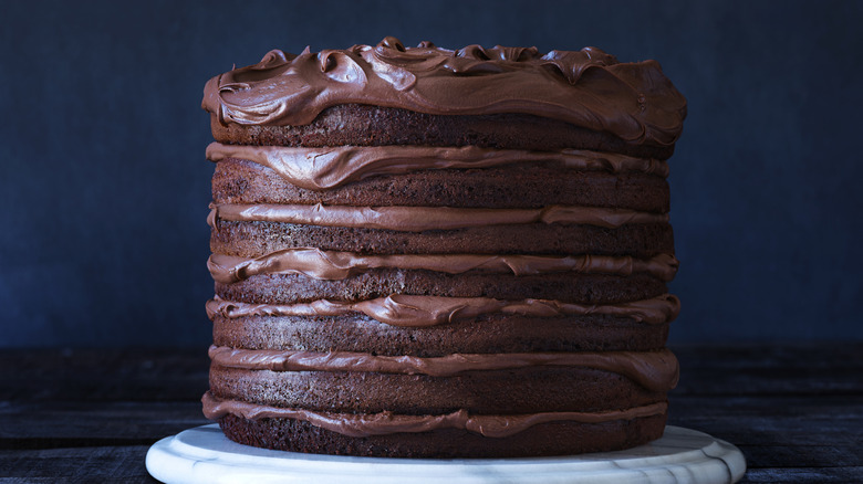 Multi-layer chocolate cake with frosting on a marble plate and dark background.