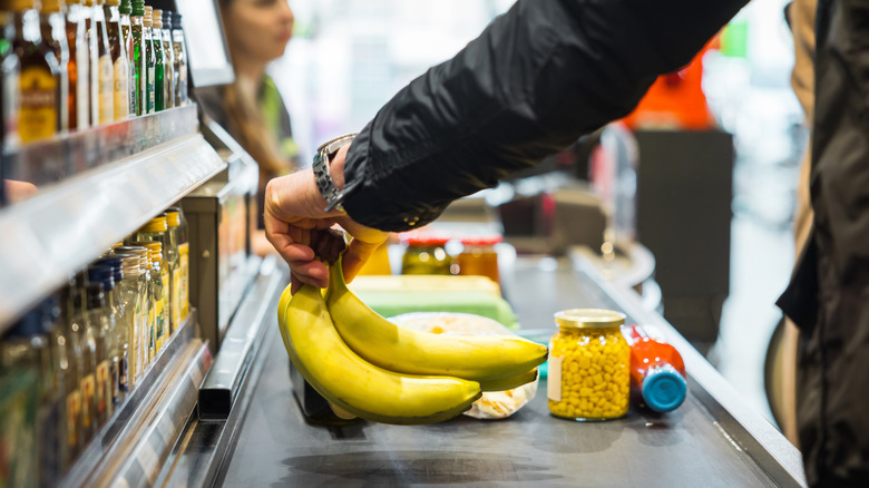 man sets bananas on grocery store conveyor belt