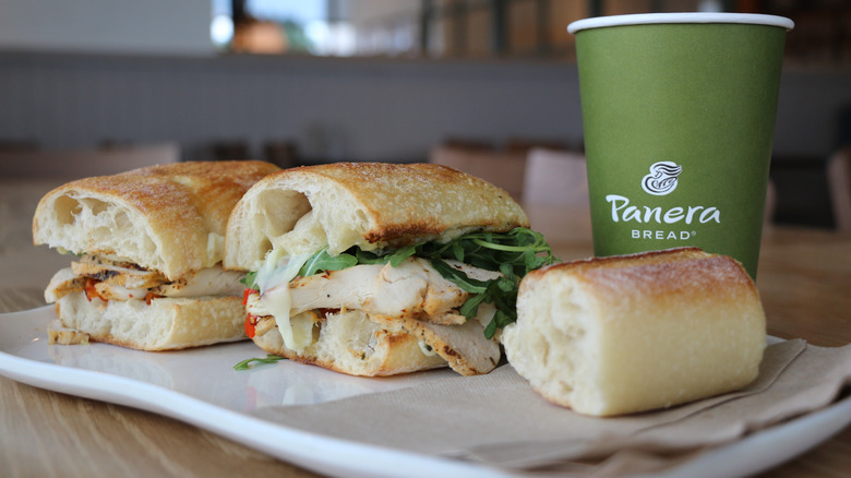 Two halves of a sandwich from Panera bread on a plate along with a cup