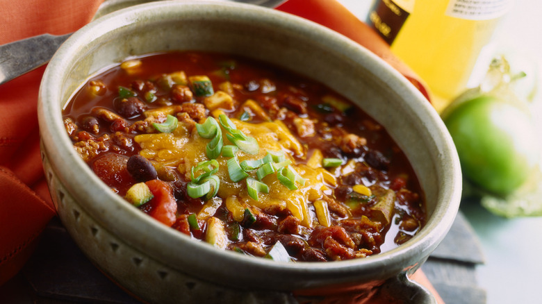 Close up of bowl of chili on a table with beer bottle in the background