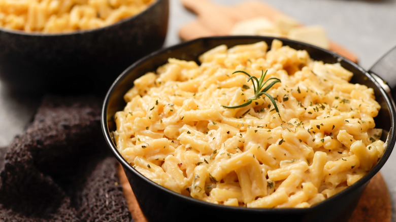 Close up of a bowl of mac and cheese on a table with another bowl of mac and cheese in the background.
