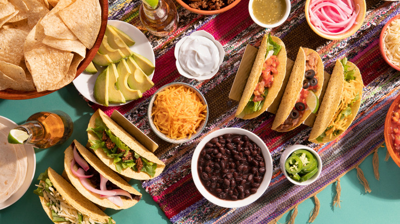 Taco bar with tortillas, cheese, beans, avocado, sour cream, peppers, beer, and other fixings.
