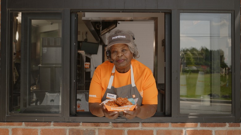 An older woman holds a basket of Popeyes wings