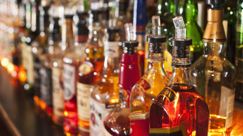 colorful bottles of liquor with pour spouts lined up on shelves behind a bar