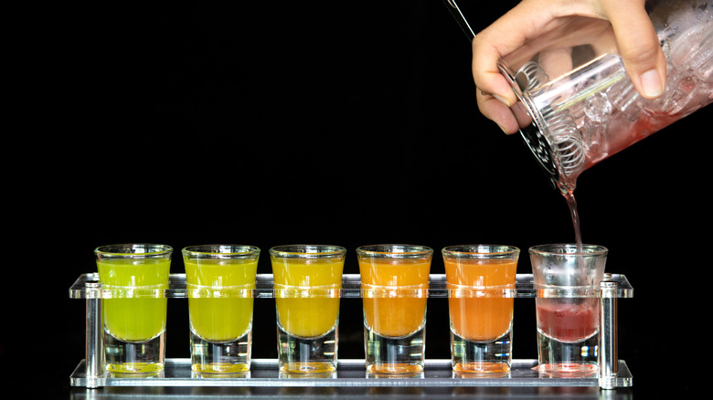 cocktail tumbler pouring liquid into colorful row of shots