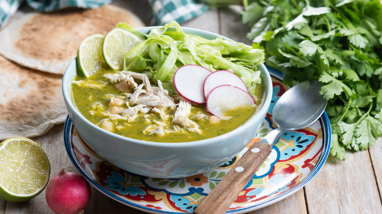 Pozole verde in bowl with spoon and ingredients